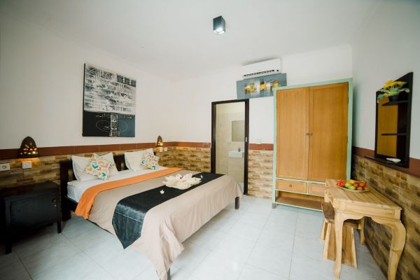 Cozy Balinese bedroom with king bed, orange bedding, wooden wardrobe, and tropical accents. - Bali Villas